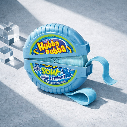 A blue Hubba Bubba bubble gum roll with a matching carrying strap, photographed on a light gray textured surface with geometric clear blocks and diagonal shadows.