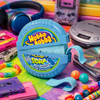 A blue retro-style Hubba Bubba bubble gum roll displayed in a colorful, vintage-themed setting with headphones, cassette tapes, a CD, beads, and bouncy balls.
