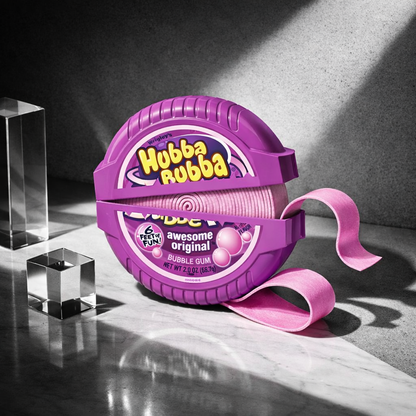 A roll of Hubba Rubba bubble gum in its signature purple plastic case, with a pink ribbon unspooling. The packaging features the yellow 'Hubba Rubba' logo and 'awesome original' text.